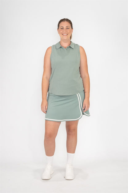Woman with mid size body wearing fairway green sleeveless golf polo and matching fairway green golf skort with sand trim, smiling and standing against white background. Elegant and functional women’s golf apparel designed for stylish and active players of all sizes.
