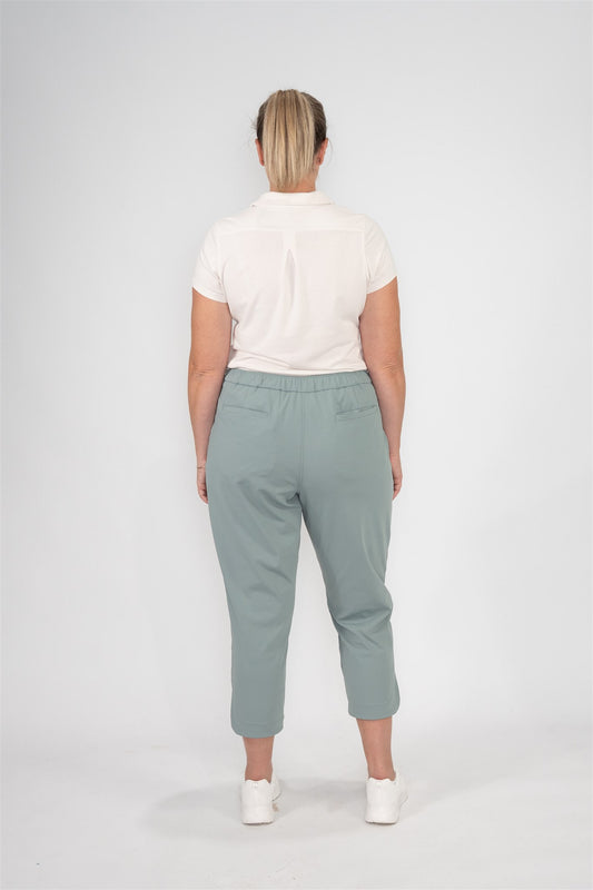 Mid-sized woman wearing Sand short-sleeve polo and Fairway Green tapered ankle golf pants, back view showing elastic waistband and welt pockets. Clean white studio setting. Elegant and functional women’s golf apparel for stylish movement and all-day comfort.