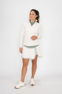 Woman wearing Fairway Green polo layered under a Sand quarter-zip pullover and Sand wrap skort with Fairway Green trim, smiling in a relaxed front-facing pose. Sleek and functional women’s golf apparel styled for lightweight layering and versatile on-course elegance.