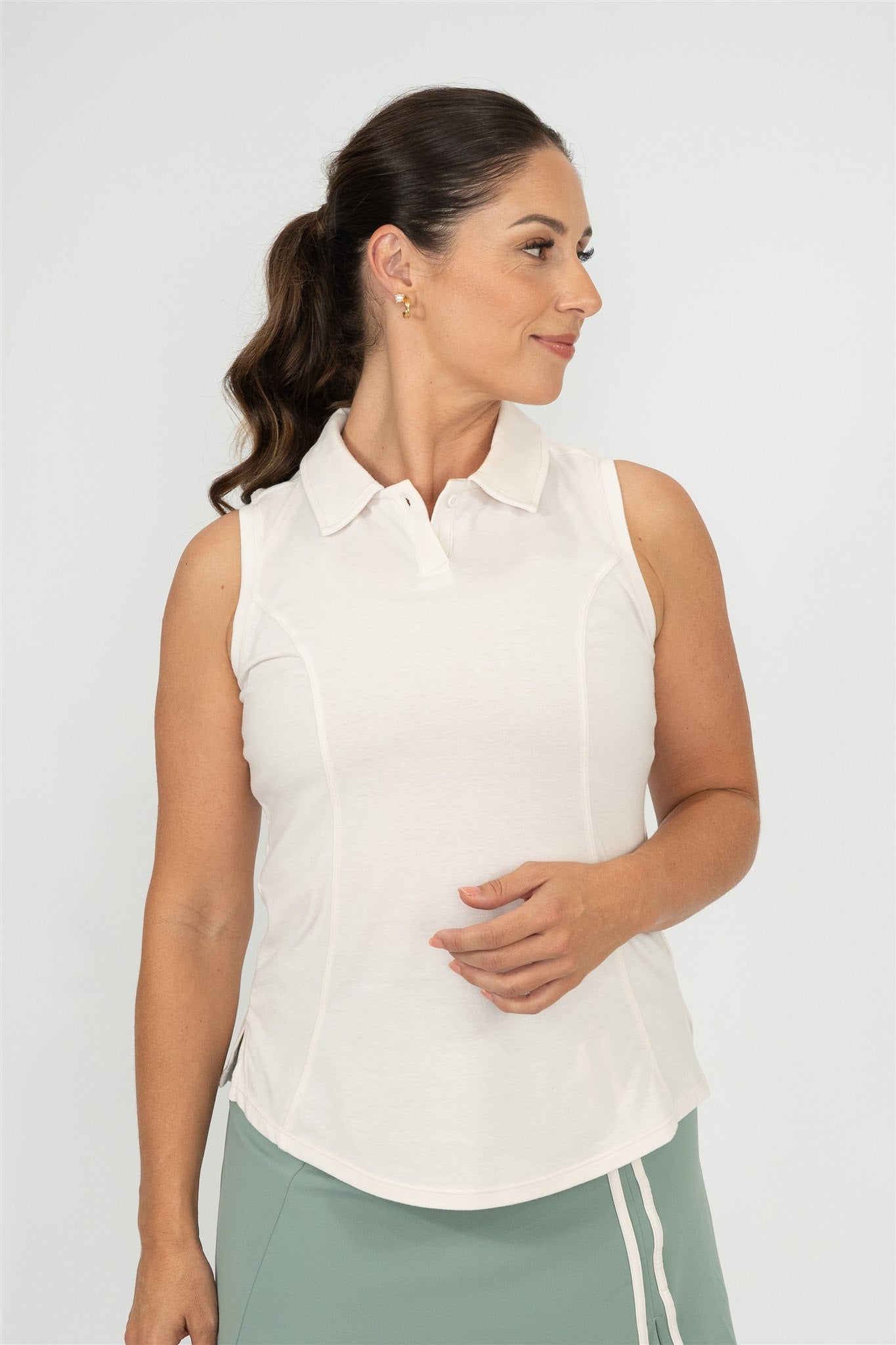 Woman wearing Sand sleeveless polo and Fairway Green wrap skort with white trim, looking to her right in a side-facing pose. Elegant and breathable women’s golf wear designed for confident, active lifestyles.