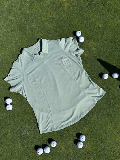 Fairway Green short sleeve women’s golf polo laid flat on grass, surrounded by golf balls. Premium, breathable fabric with elegant seam detailing designed for stylish performance on the course.