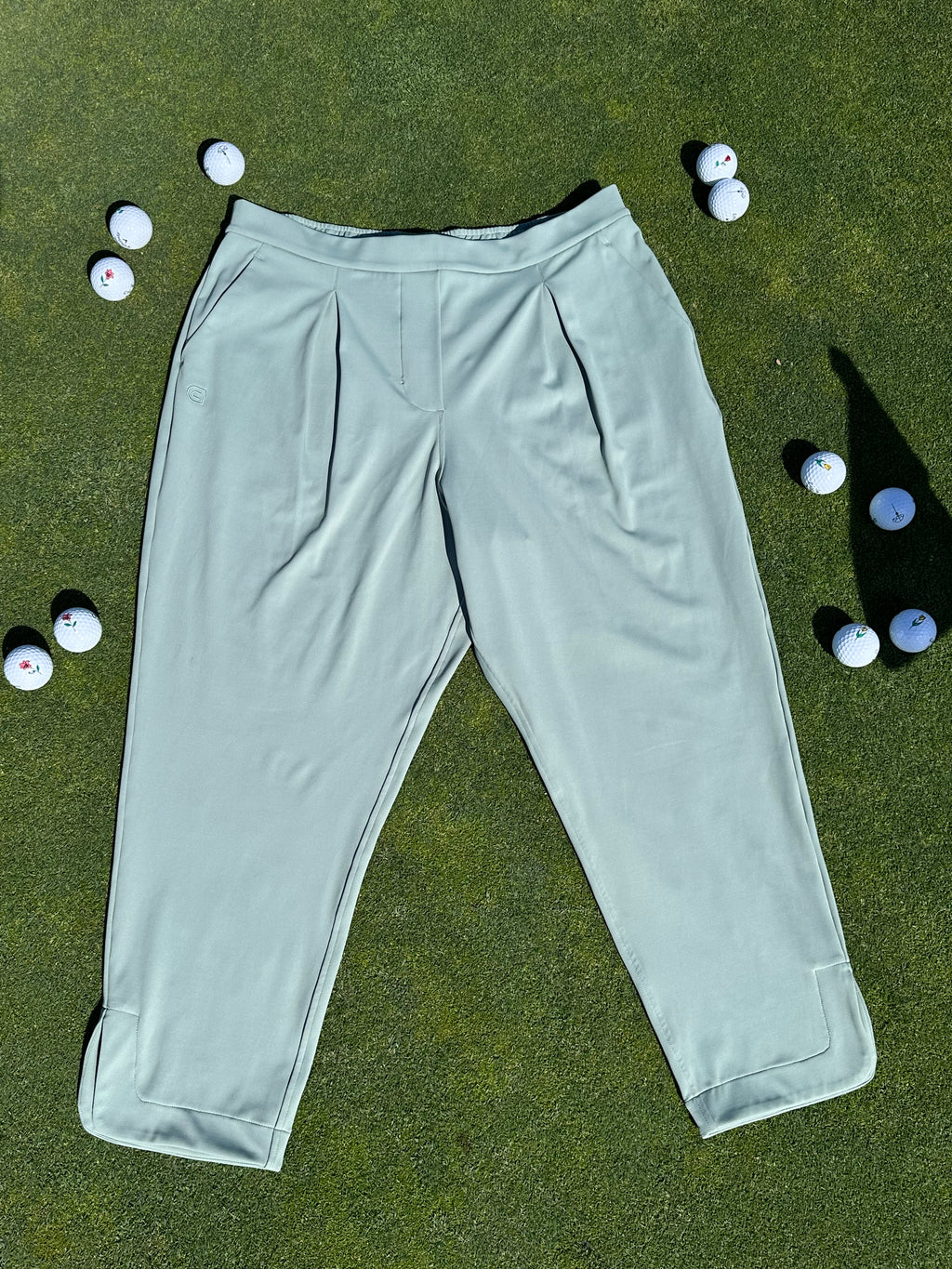 Fairway Green ankle-length golf pants laid flat on the green surrounded by scattered golf balls. Elegant and functional women’s golf apparel designed for movement and style.